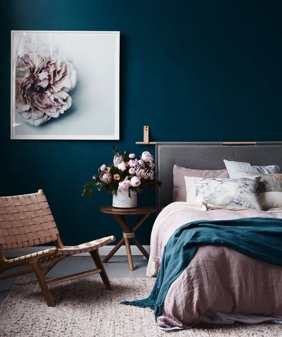 Quarto de casal combina a parede azul escura com o branco e o rosa suave na cama e nos objetos