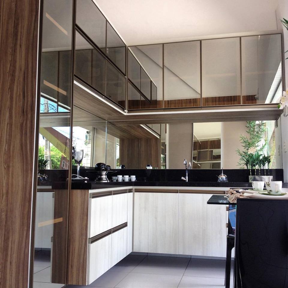 O acabamento bronze da porta de vidro em conjunto com os detalhes escuros dessa cozinha.