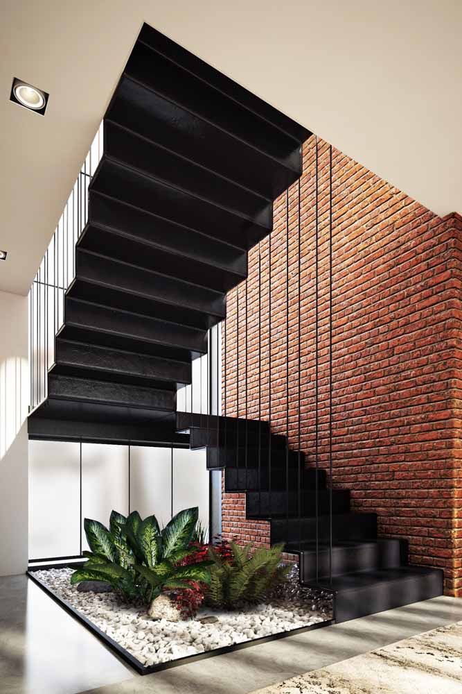 Combinação entre o moderno e o sofisticado presente na escada preta com o rústico da parede de tijolinhos