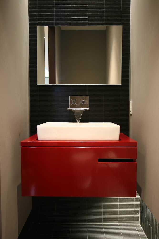 O banheiro de bancada vermelha e parede preta ganha destaque com a luz difusa