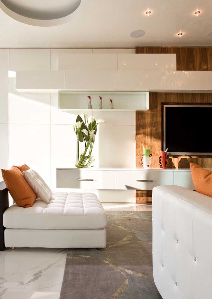 O branco é a cor que predomina nessa sala de estar moderna; os tons quentes de laranja e o amadeirado ajudam a deixar o ambiente mais acolhedor