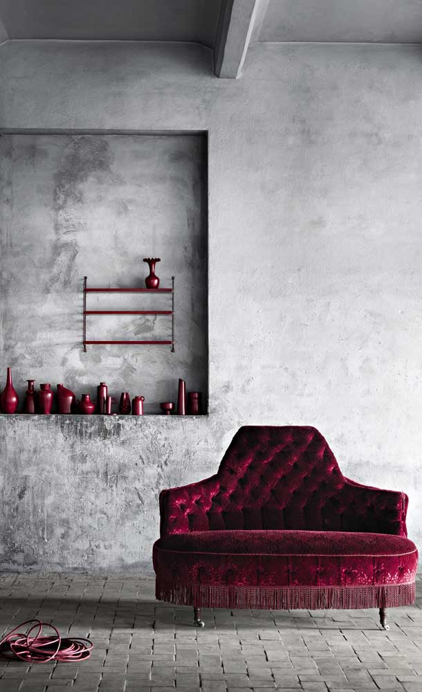 Ousadia e sensualidade nesse sofá vermelho Borgonha estilo Luis XV; repare no contraste com o ambiente moderno em cimento queimado
