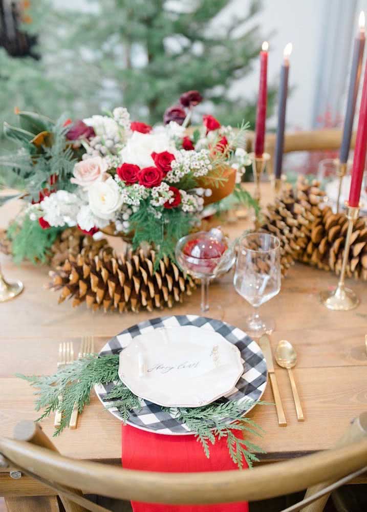 Mesa de Natal elegante com arranjo de flores e pinhas. Prepare ainda um jogo de pratos e talheres especiais para a ocasião.