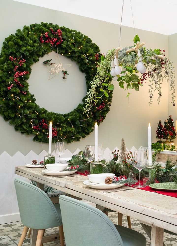 Mesa de jantar de Natal alinhada a uma grande guirlanda. Aqui até o lustre foi enfeitado para entrar no clima da comemoração