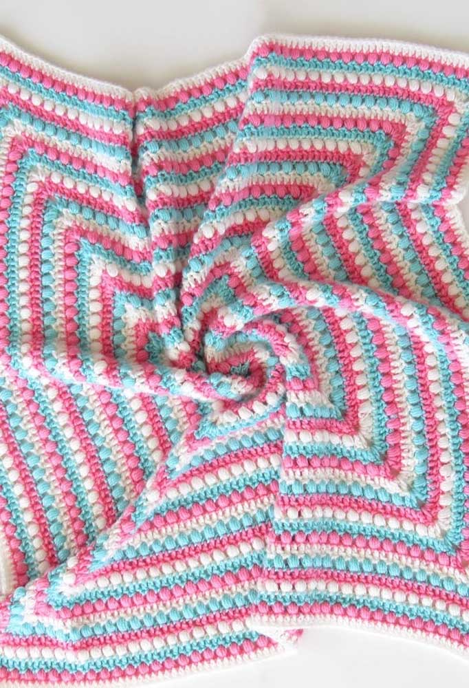 Peça multicolorida de crochê em tapete de barbante rosa, azul e branco.
