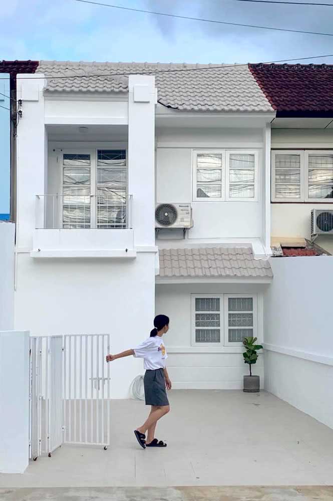 Casa simples branca com dois pavimentos e portão baixo.
