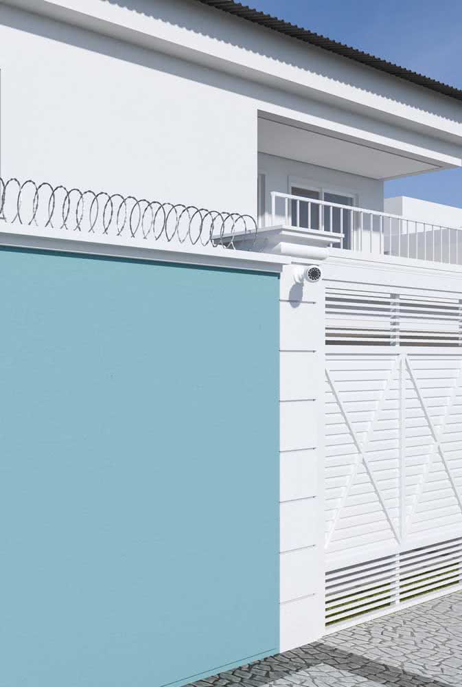 Fachada de casa com muro azul e portão branco metálico. Varanda no pavimento superior.