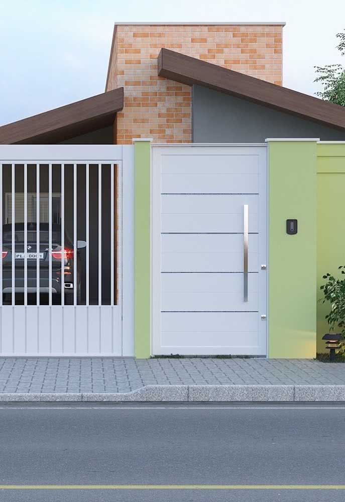 Fachada de casa simples térrea com muro verde, portão grande da garagem e portão lateral na cor branca.