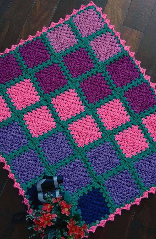Tapete de crochê quadriculado com bordas verdes, rosa e quadrados de diferentes cores.