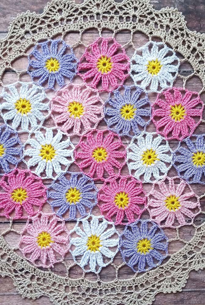 Centro de mesa com diversas flores de crochê: rosa, lilás e brancas com centro amarelo.