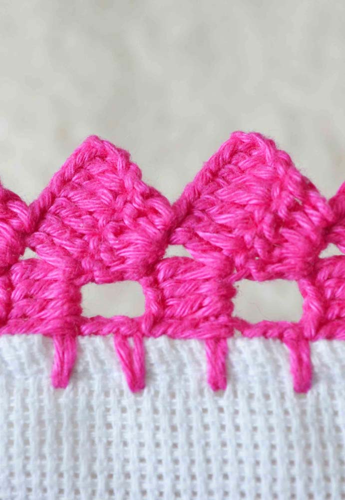 Belo e delicado bico de crochê cor de rosa para uma peça artesanal branca.