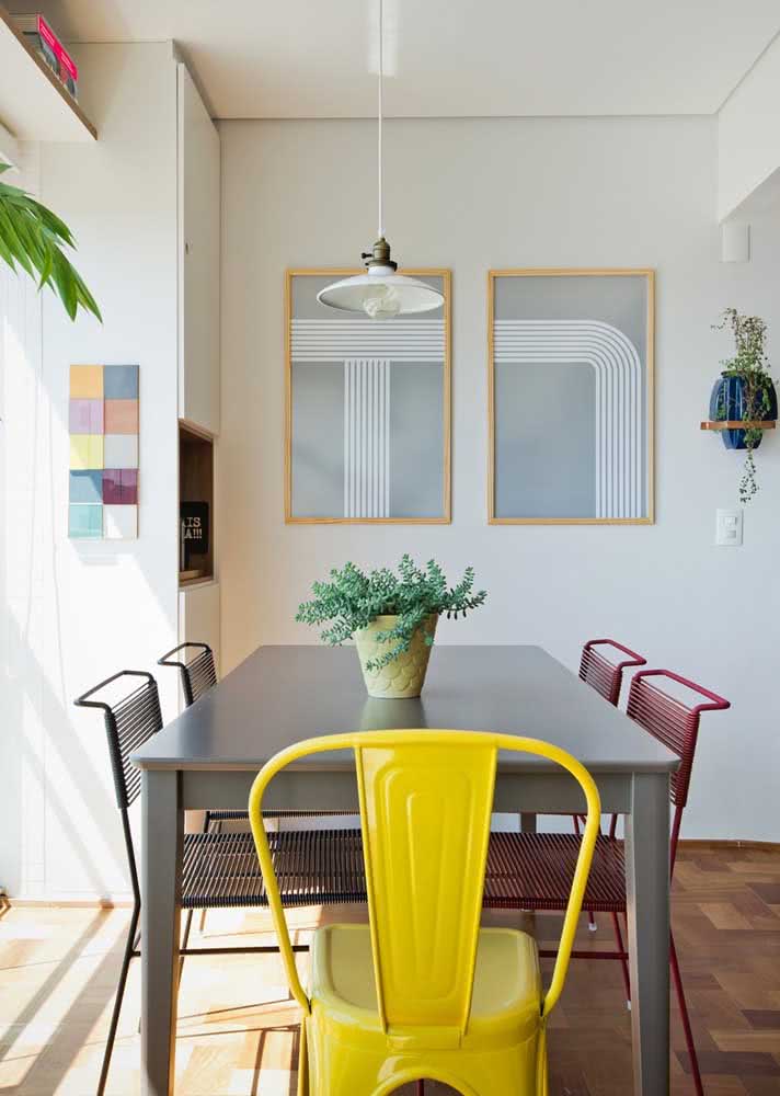 Sala de jantar com cadeiras metálicas e de fio juntas. Cada uma com uma cor.