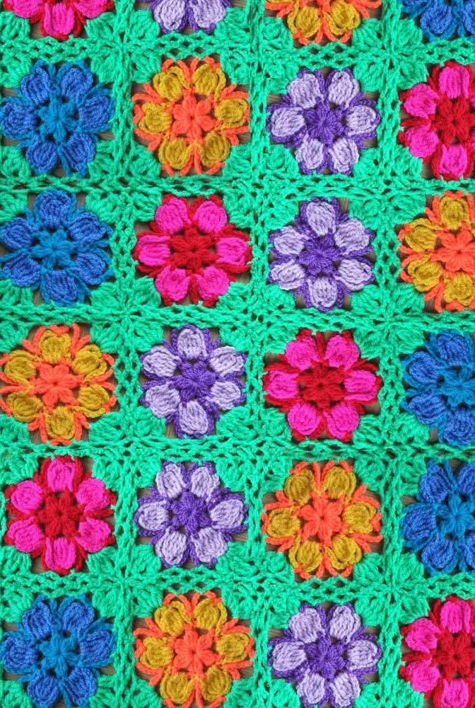 Tapete de crochê com flores coloridas e bordado verde ao redor.
