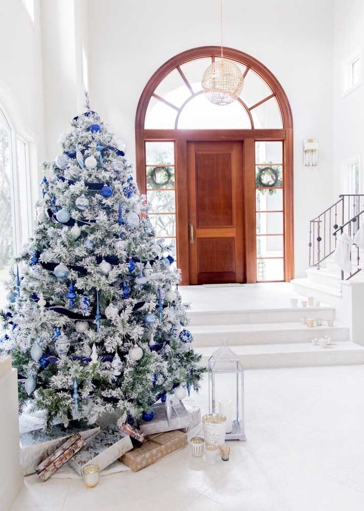 Árvore de Natal branca e verde com enfeites na cor azul na entrada da residência.