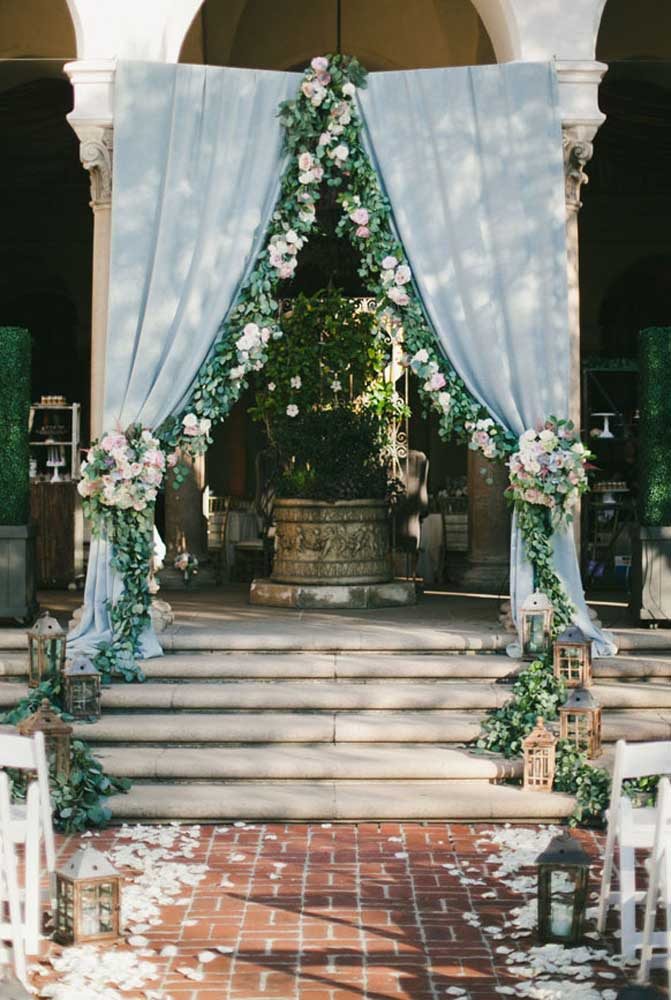 Muito charme no altar com tecido azul para cortina toda florida e trabalhada para uma cerimônia perfeita.