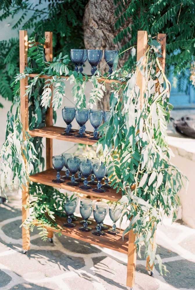 Prateleira decorada com taças azuis e muitas folhas.
