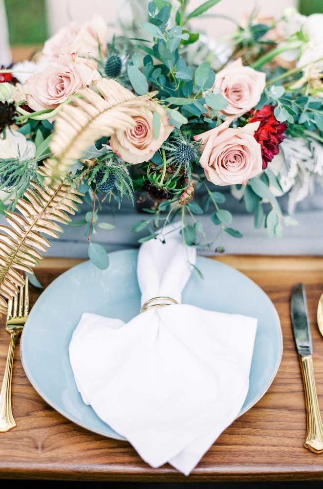 Detalhe da mesa dos convidados: prato azul claro com talheres dourados.