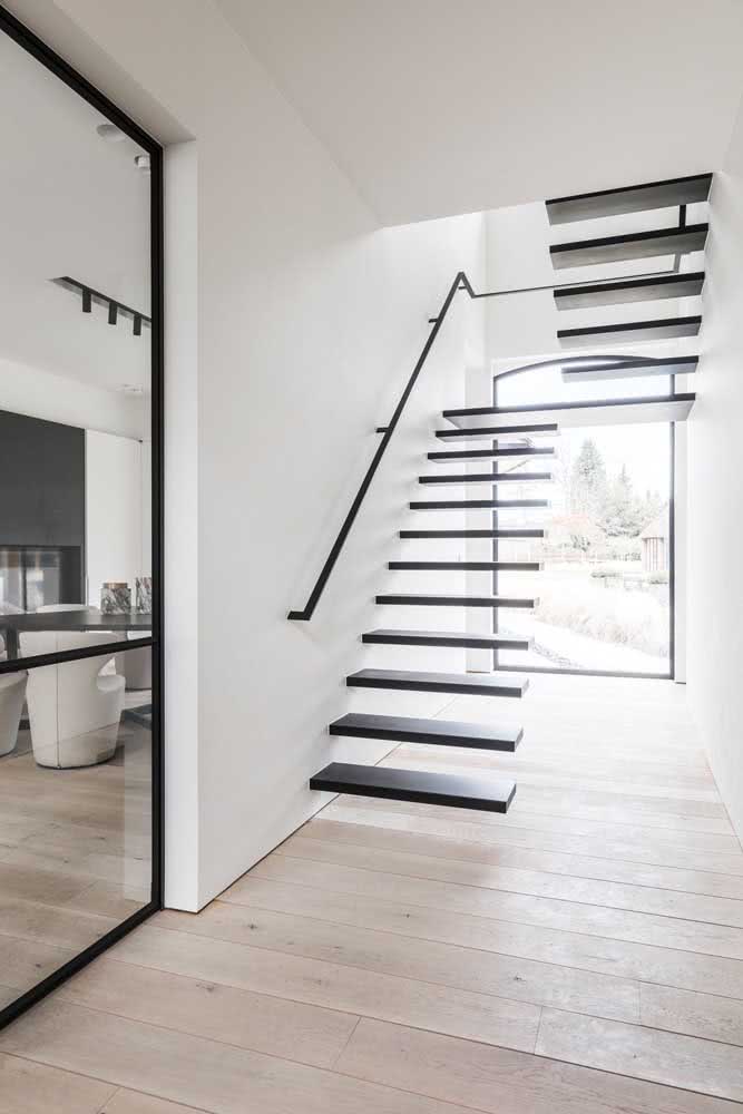 Escada flutuante com degraus pretos em contraste com a parede branca. Uma ótima pedida para ambientes minimalistas