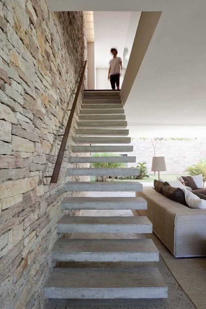 Escada flutuante de concreto na parede de pedras rústicas: uma combinação perfeita