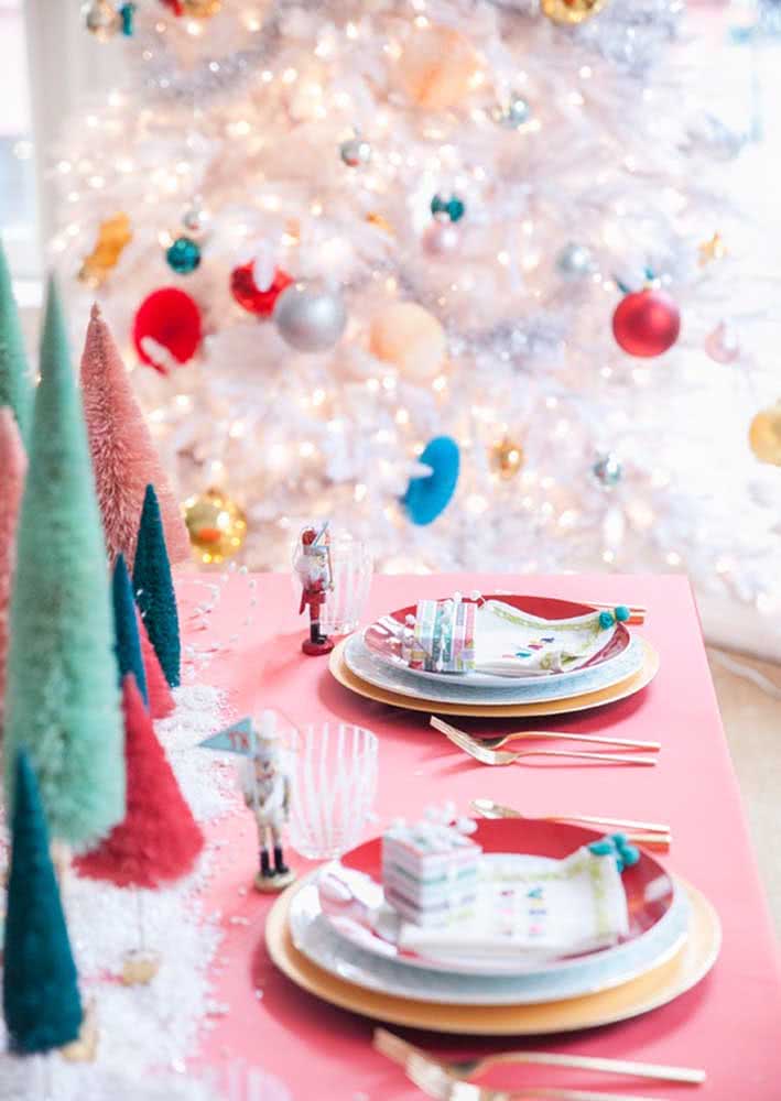 Mesa de Natal rosa com pequenos bonecos e árvores coloridas.