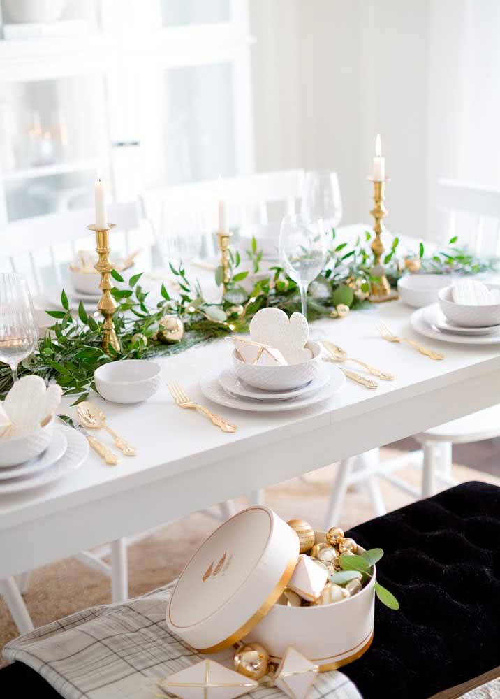 Decoração de Natal com metais dourados e ramos de folhas no centro da mesa.