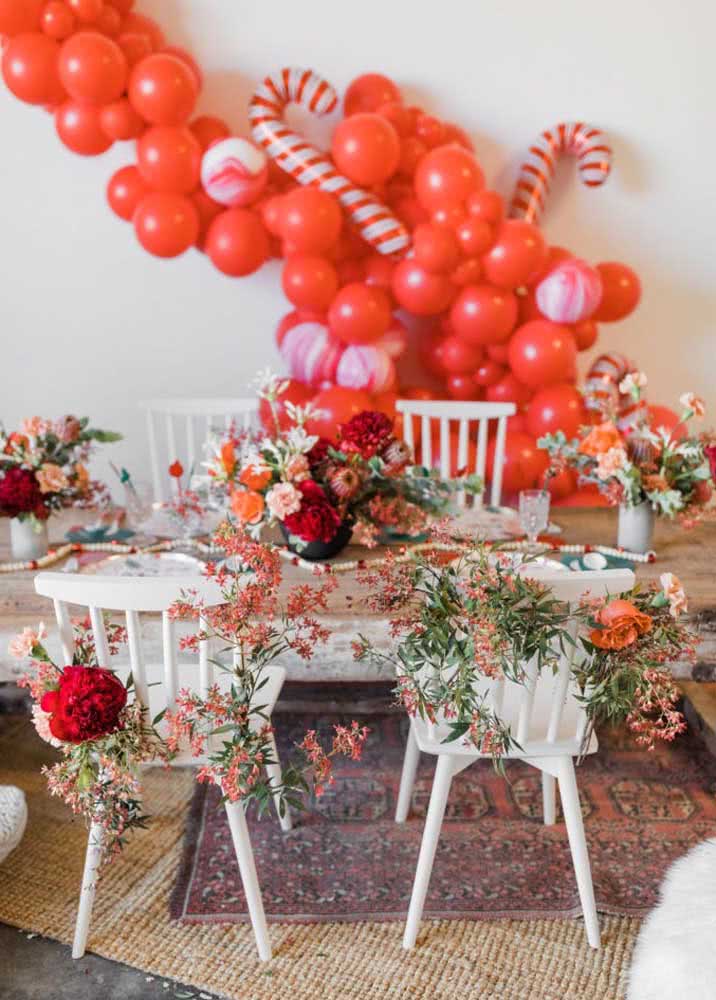 Mesa de Natal com muitas flores e arco de balões vermelho no fundo.