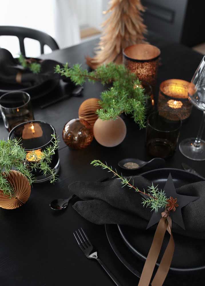 Decoração de mesa de Natal elegante e intimista em uma mesa preta, com pratos e guardanapos também seguindo a mesma cor.