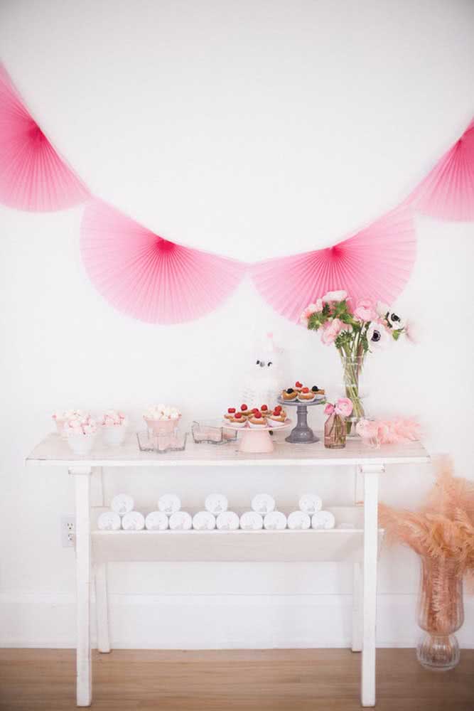 Varal com leques rosas e mesa simples com doces.