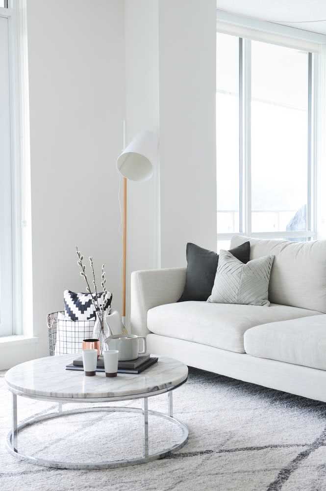 Sala de apartamento minimalista com tapete, mesa de centro, luminária e sofá.