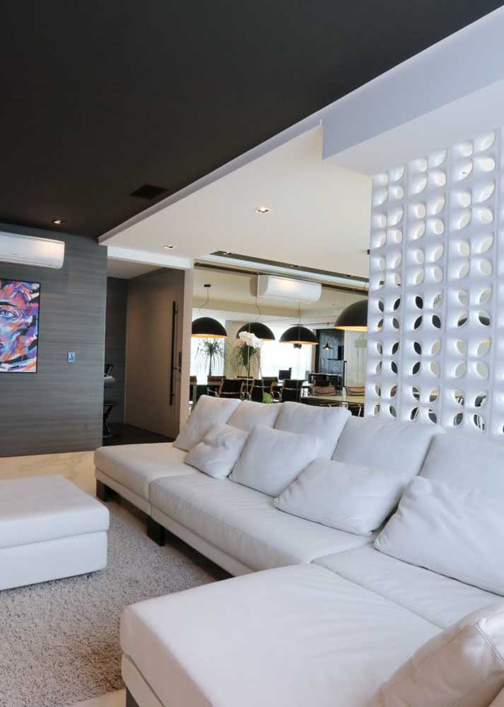 Sala de estar com cobogós brancos e sofá branco.