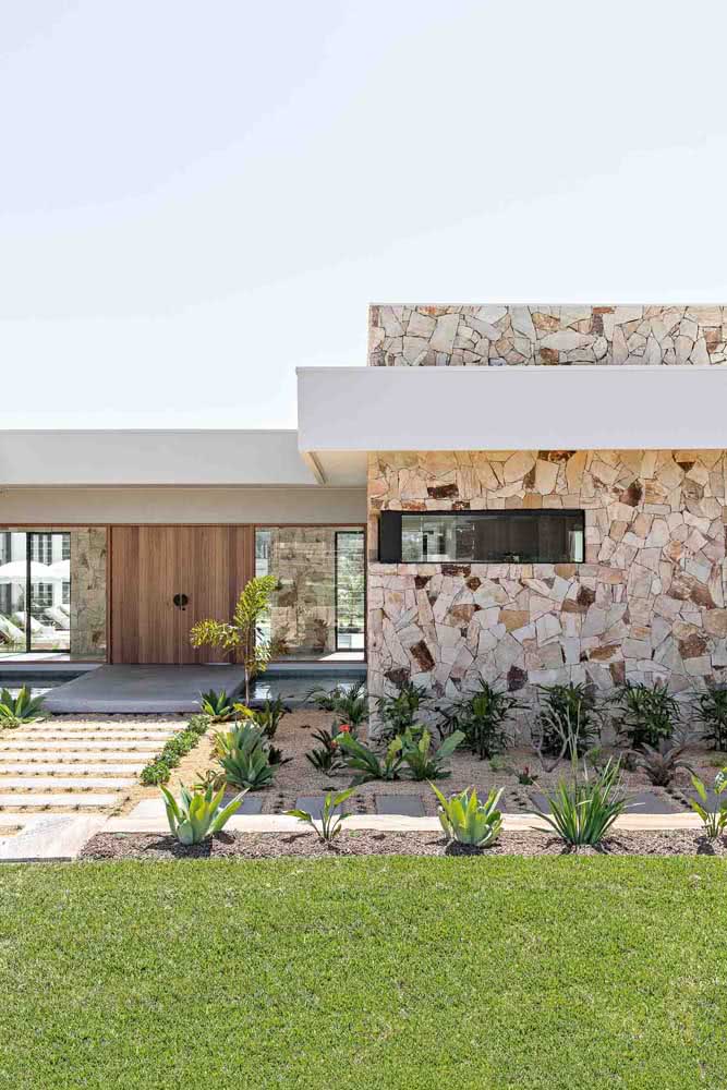 Fachada de casa térrea com pedras e projeto de paisagismo.