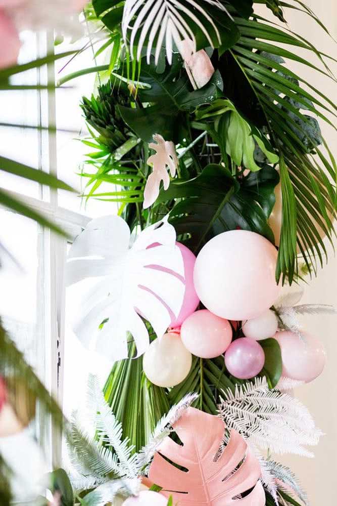 Detalhe de um vaso grande com folhas naturais, artificiais coloridas e balões para festa tropical.