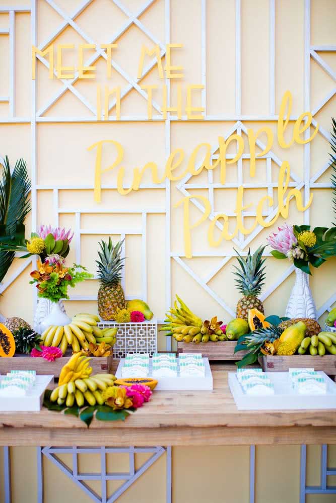 Mesa tropical com letreiro personalizado e muitas frutas a disposição dos convidados.
