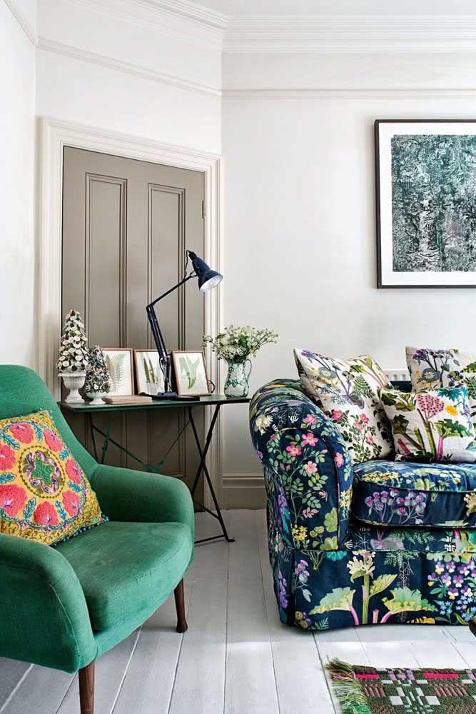 Sofá estampado floral com almofadas. Do lado, uma poltrona verde no mesmo tom que aparece na estampa