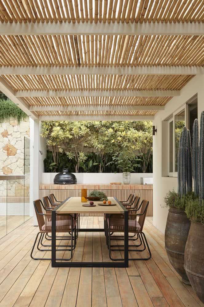Decoração de varanda grande e rústica. O teto é de bambu e o piso é de madeira