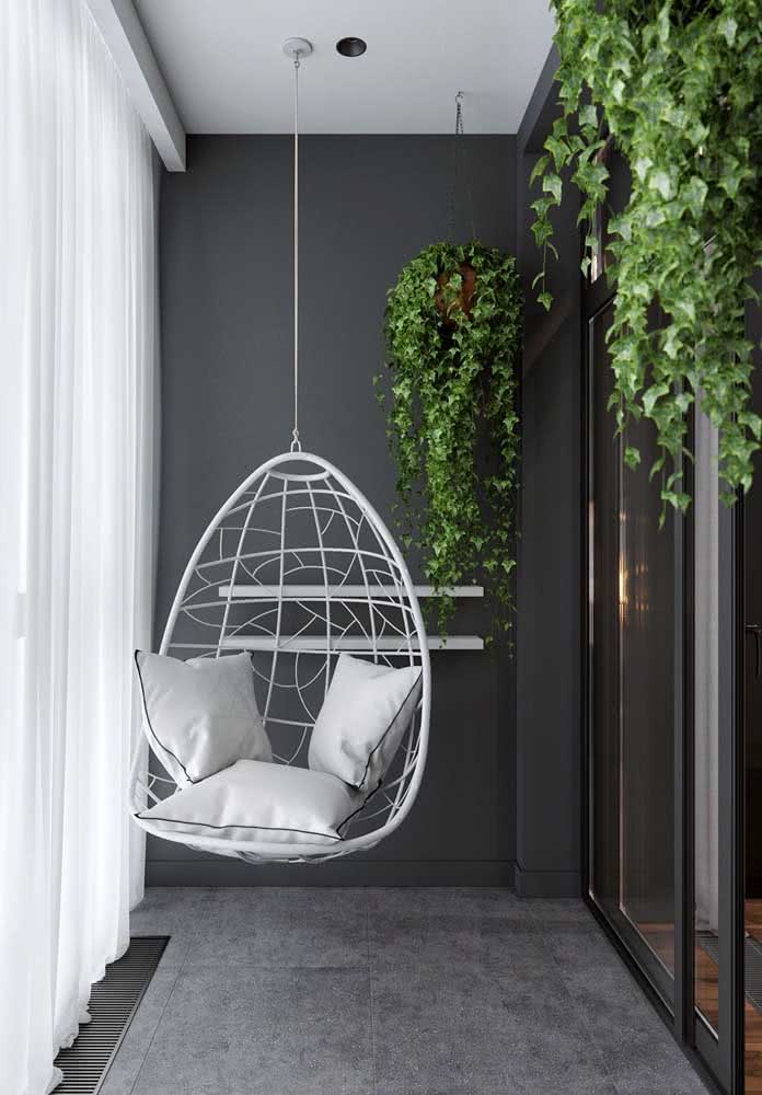 Algumas plantas suspensas, paredes pretas e uma cadeira suspensa. Está pronta a decoração da varanda pequena
