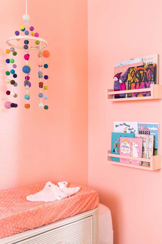 Livros e um mobile de pompom são o destaque entre os enfeites desse quarto de bebê feminino