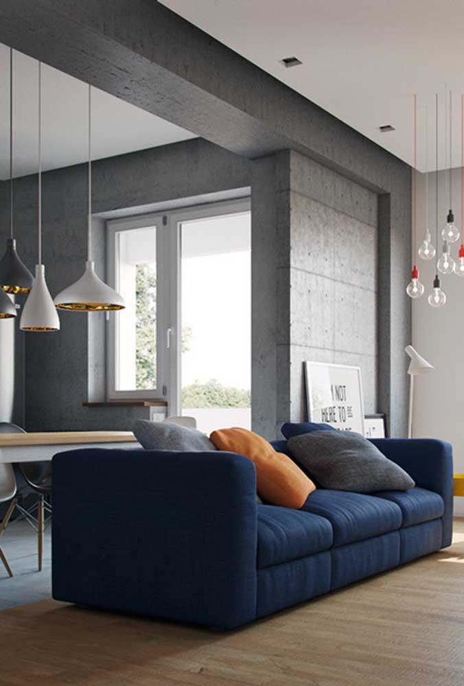 A parede de concreto aparente formou um lindo contraste com o sofá azul marinho
