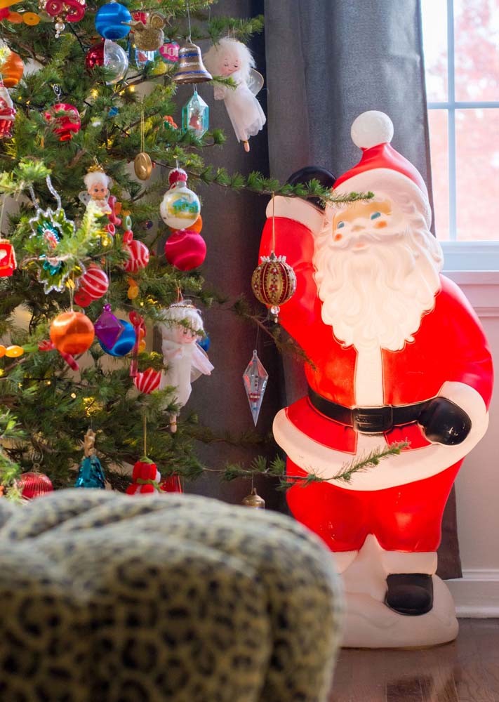 Detalhes da árvore de Natal que conta com anjinhos, sinos, bolas e um grande papai noel ao lado.