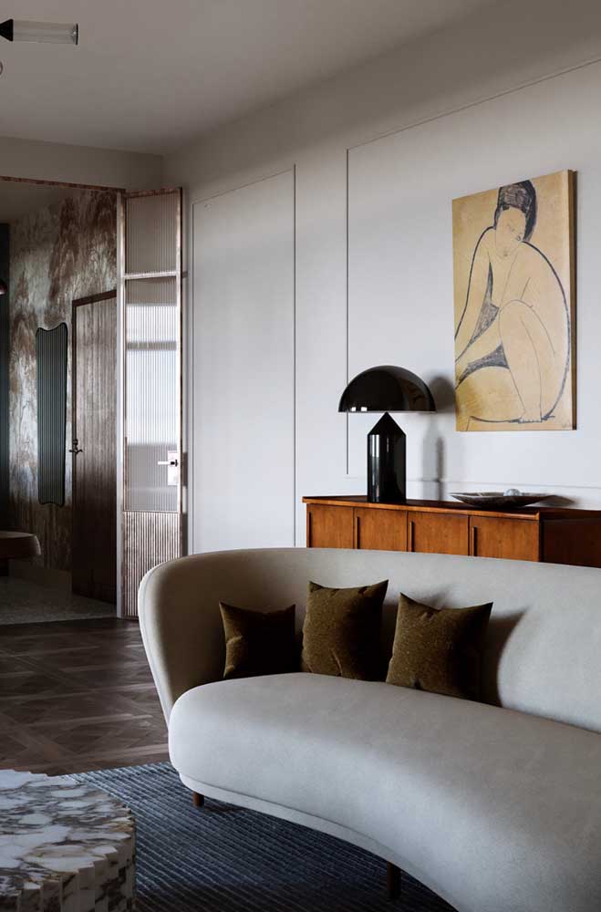 Repare como o sofá curvo forma uma bela harmonia com o quadro da mulher na parede. Ambos exibindo contornos sinuosos e orgânicos 