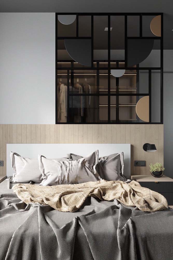 Separação da cama com cabeceira e do closet com parede de gesso e vidro.