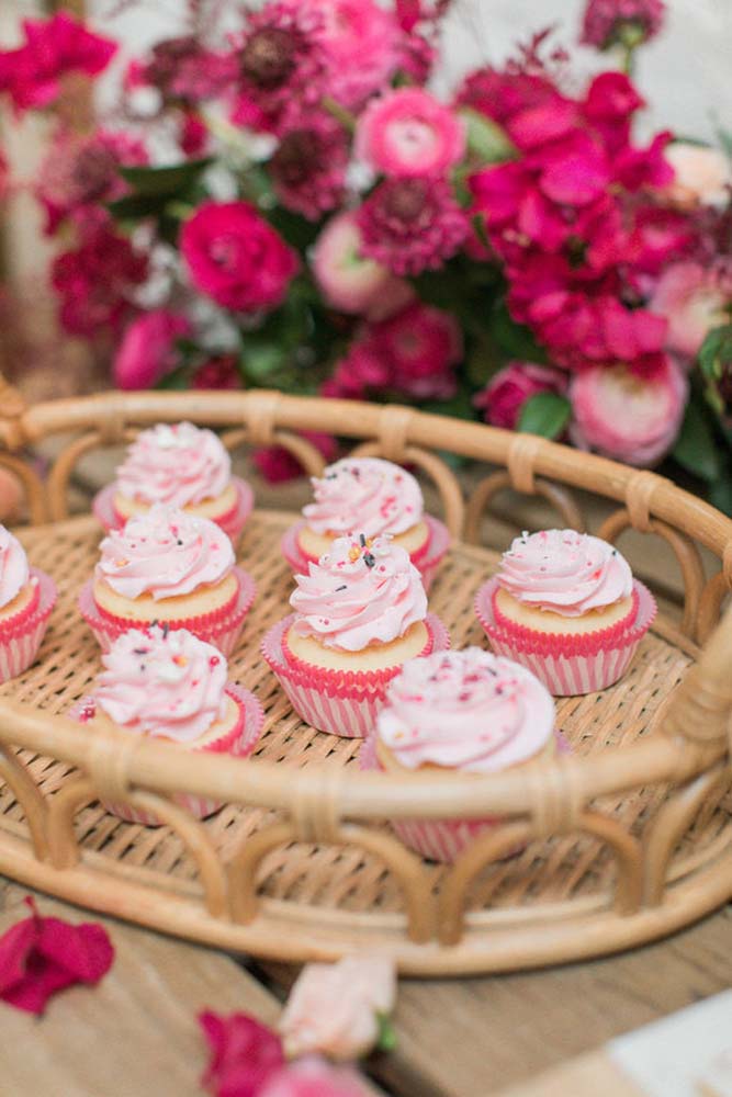 Cupcakes femininos em cesta de palha e arranjo de rosas.