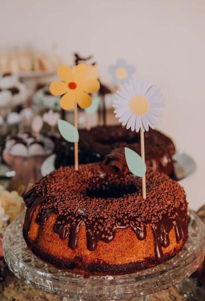 Flores de papel no palito para decorar um bolo caseiro com calda de chocolate.