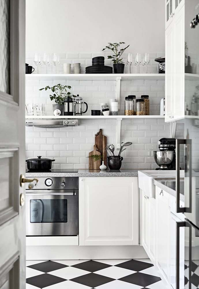 Cozinha em L branca com bancada de pedra, azulejos subway tiles e prateleiras de madeira.