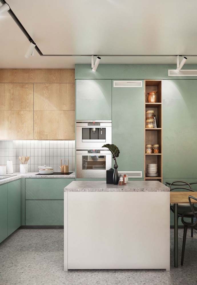 Modelo de cozinha em L com armários na cor verde água, bancada central e azulejos brancos.