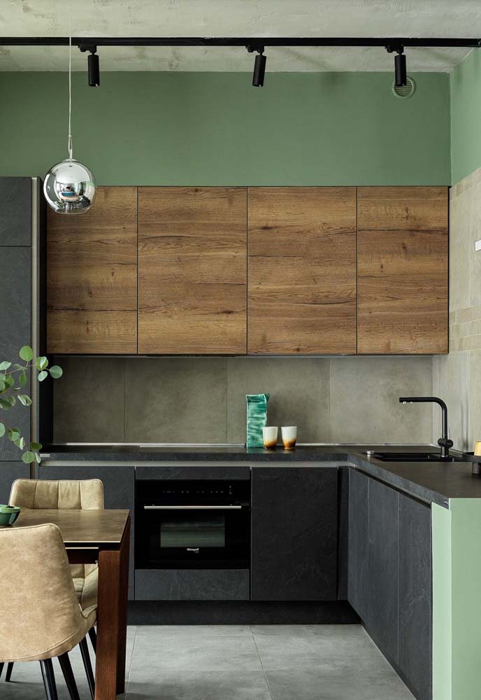 Cozinha em L verde com bancada de granito preto, armários com portas pretas na parte superior e porta de madeira nos armários superiores.