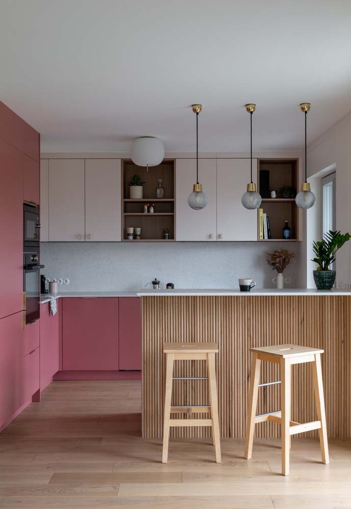 Linda cozinha rosa em L com duas tonalidades da cor nos armários e bancada de pedra branca.