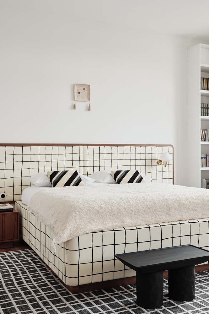 Quarto minimalista com pintura branca, cabeceira de tecido quadriculada e roupa de cama que segue o mesmo padrão.