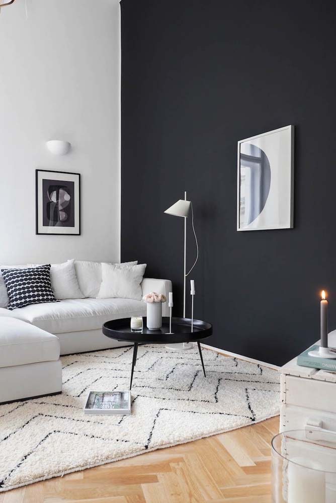 Sala preta e branca com quadros e sofá em L bem minimalista.