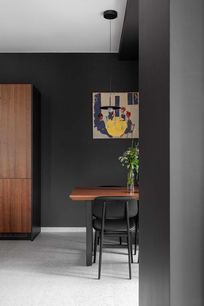 Decoração de sala com pintura preta nas paredes e móveis de madeira: armário e mesa de jantar.